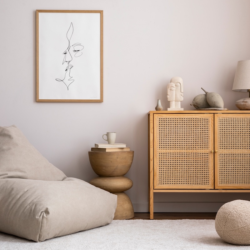 Domestic and cozy interior of living room with mock up poster frame, design pouf, lamp, decoration, wooden side table and beige accessories. Creative home decor. Template.